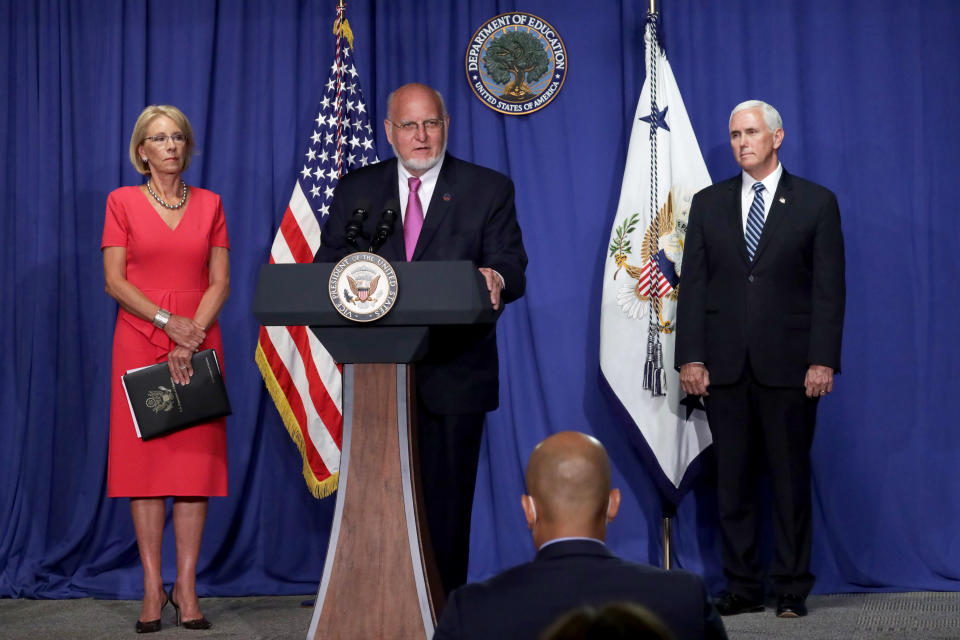 CDC Director Robert Redfield, Secretary of Education Betsy DeVos, and Vice President Mike Pence stand behind a podium at a press conference.