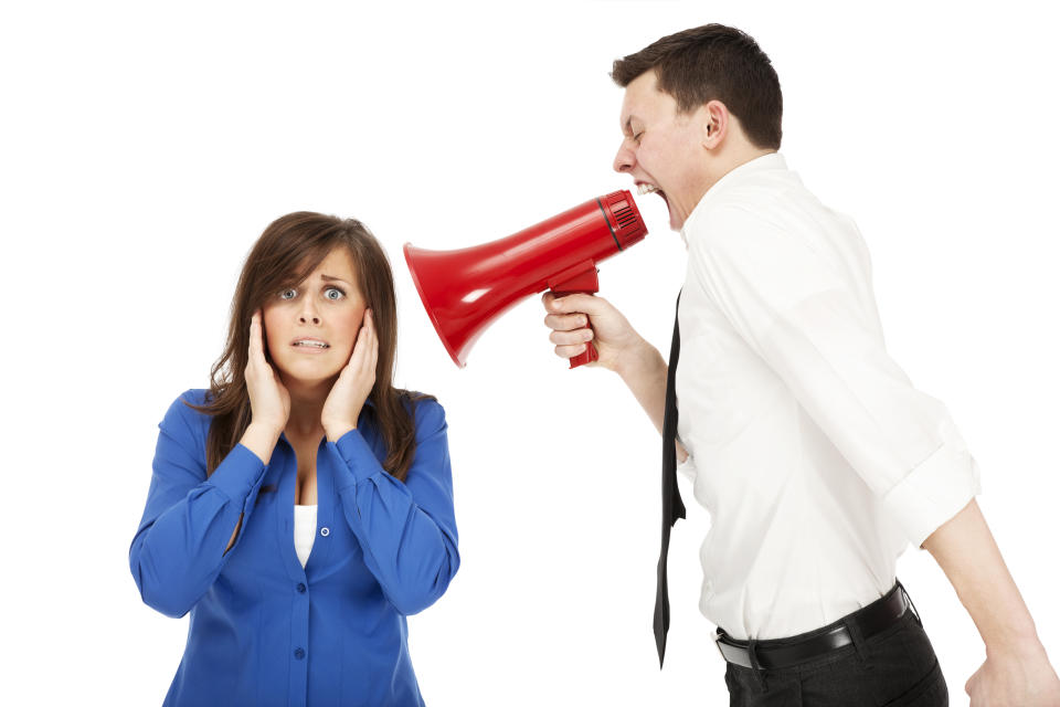 Photo of a very angry businessman screaming at a female employee through a red bullhorn.