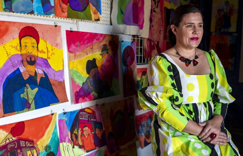 Karla Diaz, wearing a bright dress with a green and black geometric print, sits before her watercolor paintings
