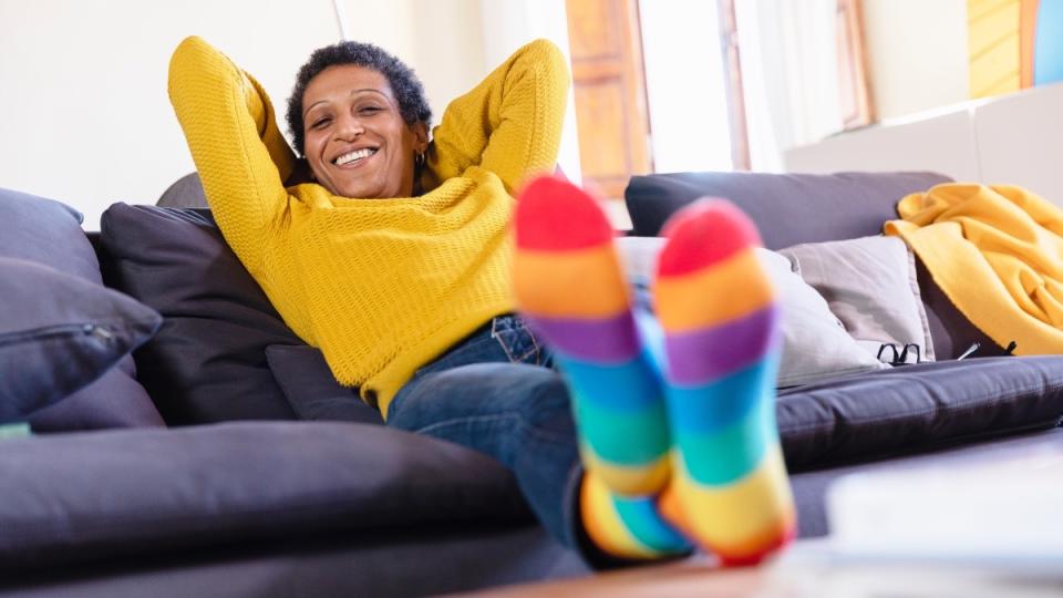 A woman relaxing on a couch with her hands behind her head while wearing colorful socks to prevent sweaty feet