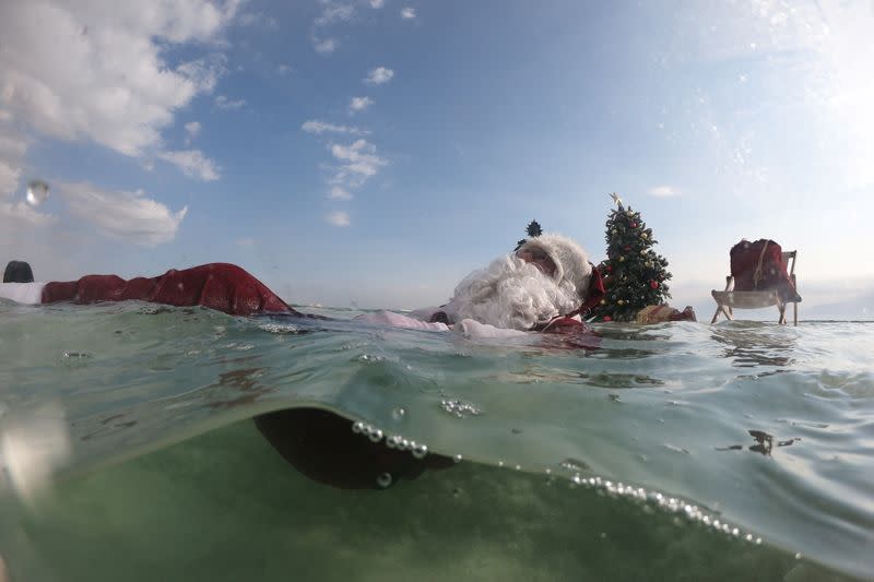 Issa Kassissieh, wearing a Santa Claus costume, floats in the Dead Sea near a Christmas tree placed on a salt formation, near Ein Bokeq