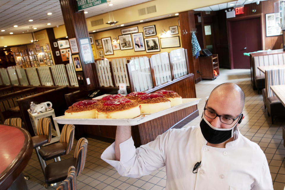 William McCarthy, the director of operations at Junior's Restaurant, delivers a tray of cheesecakes to a front counter, Monday, June 29, 2020, in New York. The Brooklyn restaurant is open for takeout service and outdoor dining only. Phase 3, allowing limited indoor dining, is scheduled to begin Monday, July 6, but Gov. Andrew Cuomo has indicated he may delay its implementation. (AP Photo/Mark Lennihan)