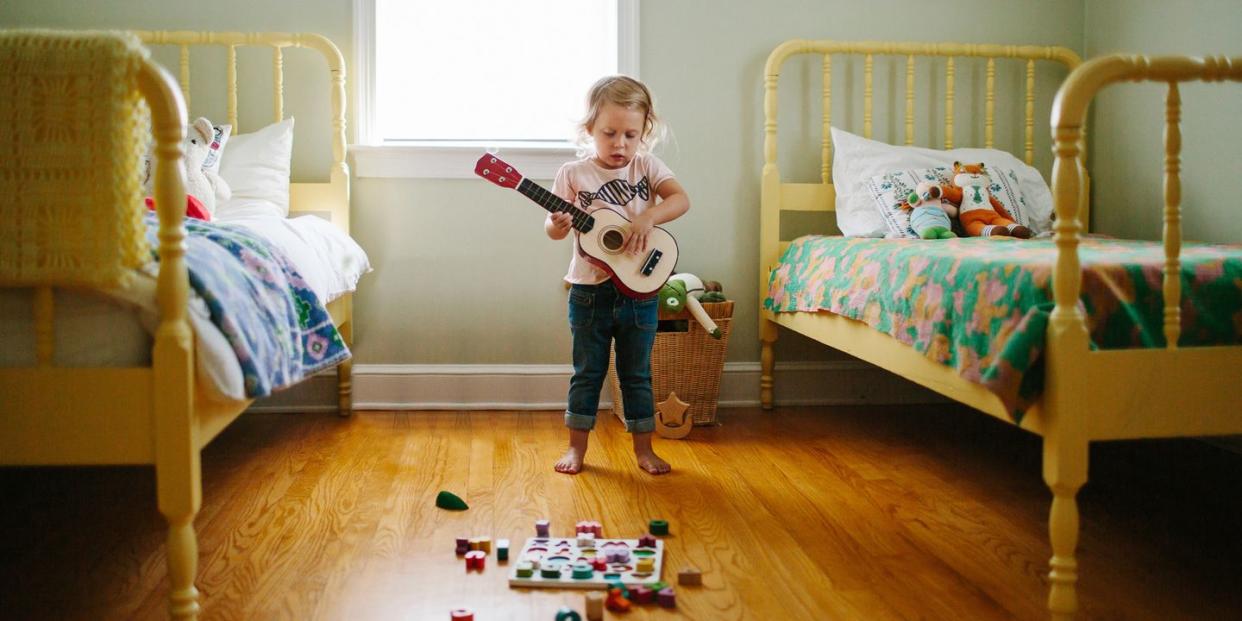 toddler playing guitar in bedroom with two yellow beds