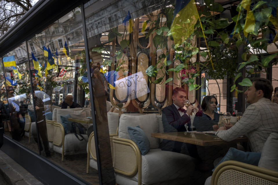 Customers drink wine inside a restaurant as demonstrators march along the street in Odessa, Ukraine, Sunday, Feb. 20, 2022. Thousands of people in Odessa marched through the streets of the city in a show of unity on Sunday, marking the date on which, eight years ago, more than a hundred people were killed during Ukraine's Maidan revolution. Waving national flags and placards with slogans such as, 'No Putin, No Cry', people said they had come out to demonstrate against a potential Russian invasion, and said that they were prepared to defend their city if needed. (AP Photo/Emilio Morenatti)