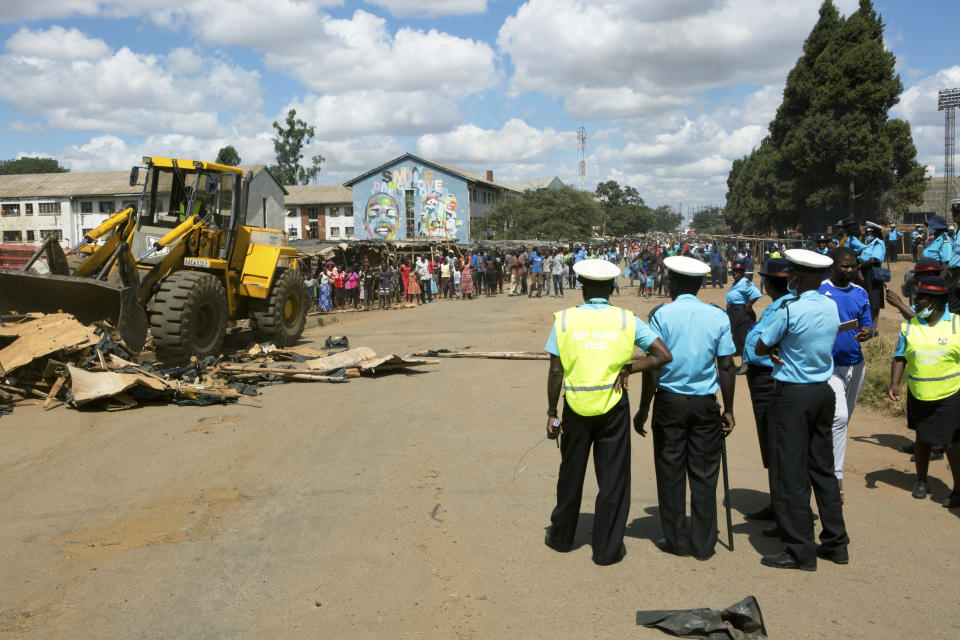 Zimbabwe council police watch as a bulldozer destroys stalls in the area of a popular market in a campaign to clean up the city, in Harare, Zimbabwe, Saturday, April 18, 2020. Zimbabwe will commemorate its 40th Independence Day under the government instructed lockdown in an effort to curb the spread of coronavirus. (AP Photo/Tsvangirayi Mukwazhi)