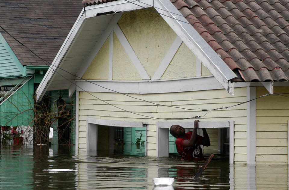 A person climbs out of a flooded house's window, surrounded by rising water, during a natural disaster scene