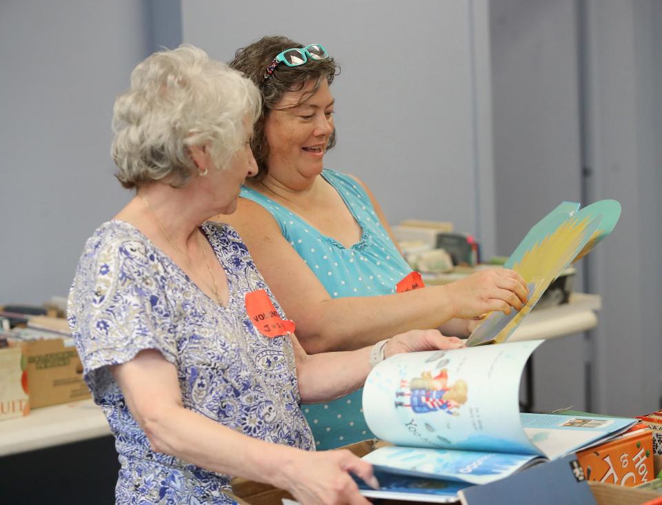 Book sale volunteers Judy Allison, left, and Leigh Ann Brown, right, look over a children's book that unfolds on Saturday, Aug. 5, 2023, at The Commons on South Linden Avenue during the Friends of Rodman Public Library's annual Used Book Sale.