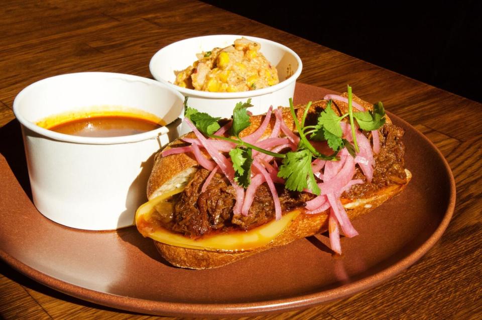 A barbacoa dip sandwich from Birote Deli in Paramount. Sides of consommé and esquites potato salad sit behind.