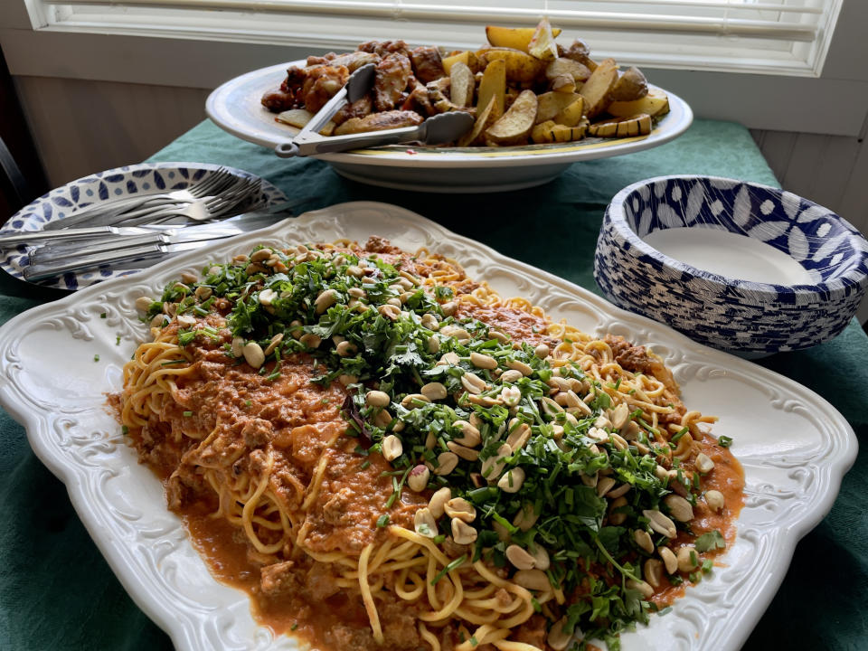 A plate of spaghetti with tomato sauce topped with herbs and nuts, served with side dishes in the background