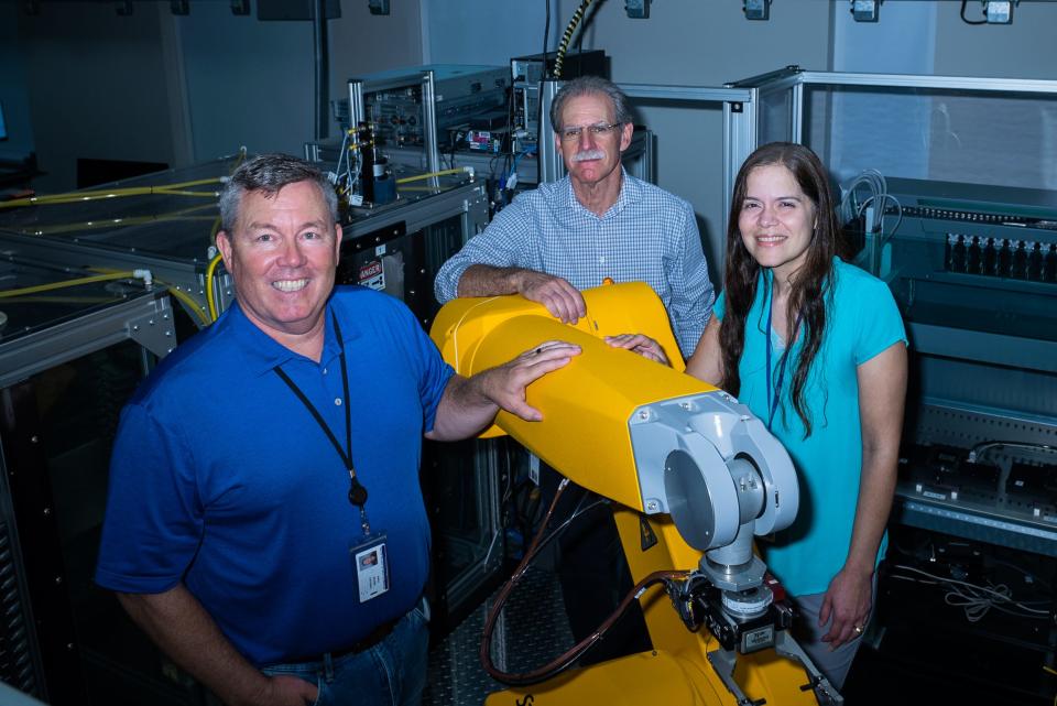 From left, Department of Molecular Medicine Senior Scientific Director Timothy Spicer, Senior Scientific Director of High Throughput Chemistry and Technologies Louis Scampavia, and High Throughput Molecular Screening Scientific Associate Virneliz Fernandez-Vega, stand next to a robotic arm platform at the Herbert Wertheim UF Scripps Institute for Biomedical Innovation & Technology in Jupiter.