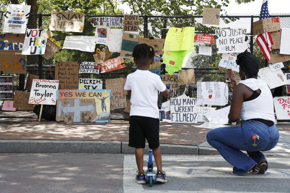 Diamond Lee of Washington, helps her son Jaylen, 4, look at signs hanging on a police fence at 16th and H Street, Tuesday, June 9, 2020, near the White House in Washington, after days of protests over the death of George Floyd, a black man who was in police custody in Minneapolis. Floyd died after being restrained by Minneapolis police officers. (AP Photo/Jacquelyn Martin)