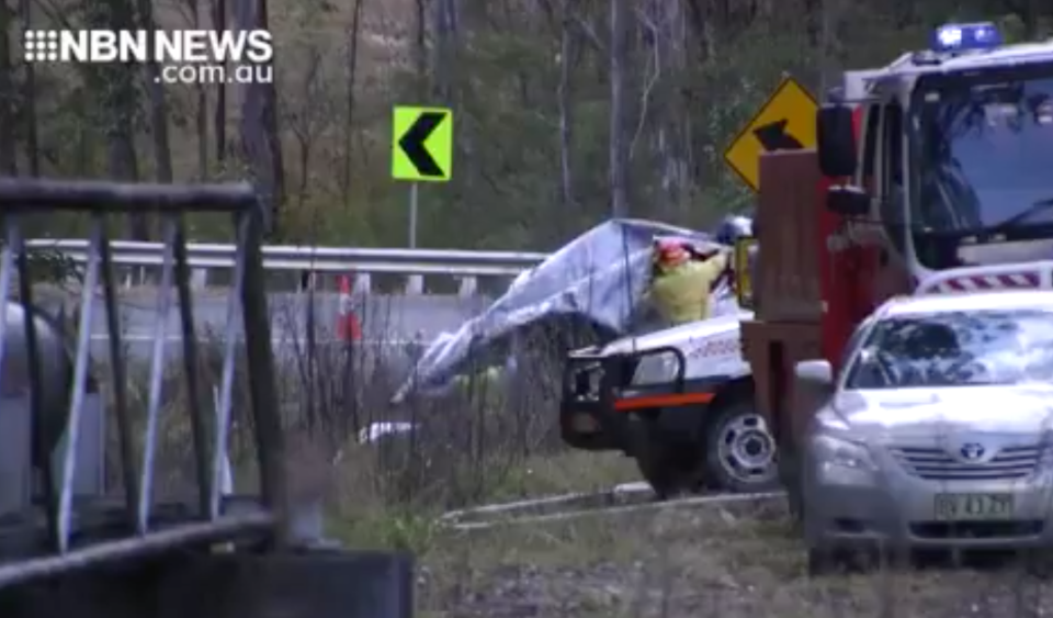 Firefighters appear to cover a car involved in the Nymboida collision, preparing to tow it away.