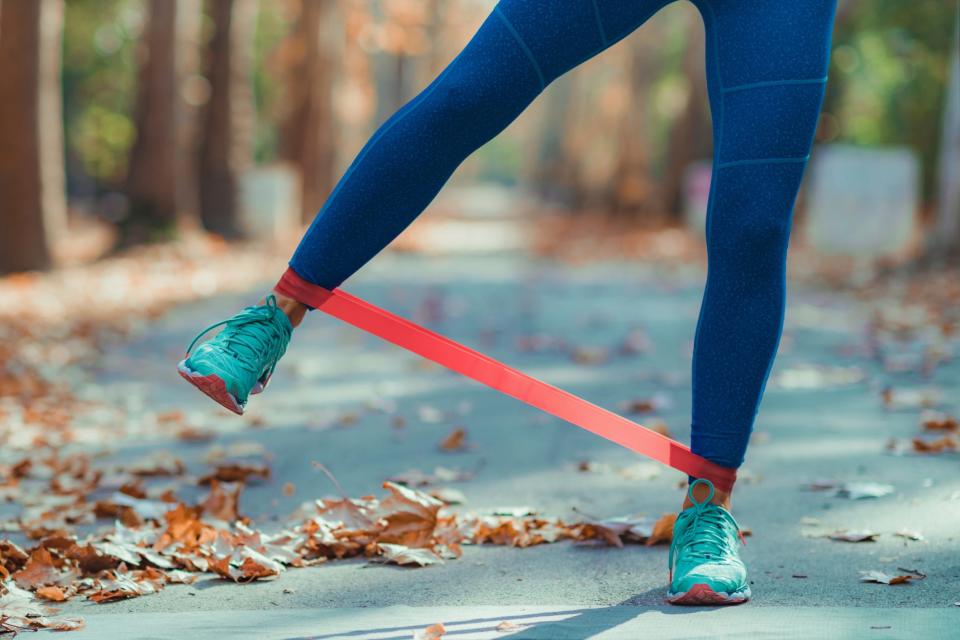 a close up of a person in workout leggings and gym shoes performing a resistance band exercise outdoors