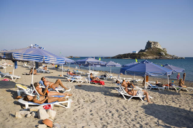 People sunbathing at Kefalos beach, Kastri island with chapel St. Nicholas in background, Kefalos, Kos, Greece