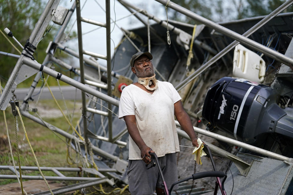 Dale Williams, who cannot speak due to a tracheotomy from cancer, stands in front of his shrimp trawler that overturned and cracked during Hurricane Ida, in Plaquemines Parish, La., Monday, Sept. 13, 2021. Ida's Category 4 winds flipped Williams' trawler on its side, bending the frame and tearing nets, but it should be ready to go after about $1,500 in repairs, he said in an interview conducted by written notes. (AP Photo/Gerald Herbert)