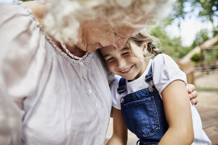 Grandparent and granddaughter hugging, girl smiling and leaning head on grandparent's shoulder