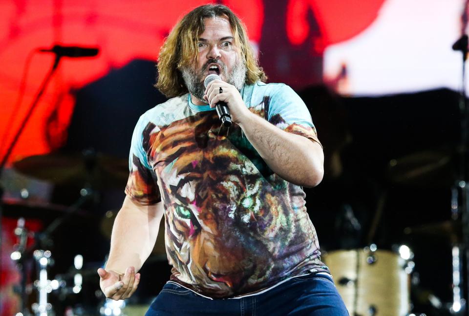 While performing on stage, Jack Black sports a T-shirt with lion head print and denim pant to match