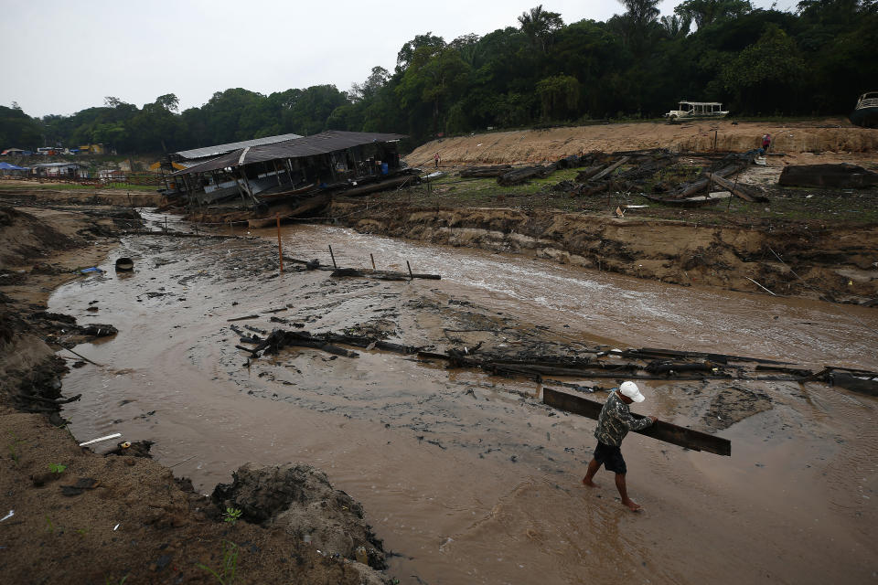 A resident carries wood to help dam up the Negro River river near his houseboat that is stuck in a dry area during a drought in Manaus, Amazonas state, Brazil, Monday, Oct. 16, 2023. The Amazon’s second largest tributary on Monday reached its lowest level since official measurements began near Manaus more than 120 years ago. (AP Photo/Edmar Barros)