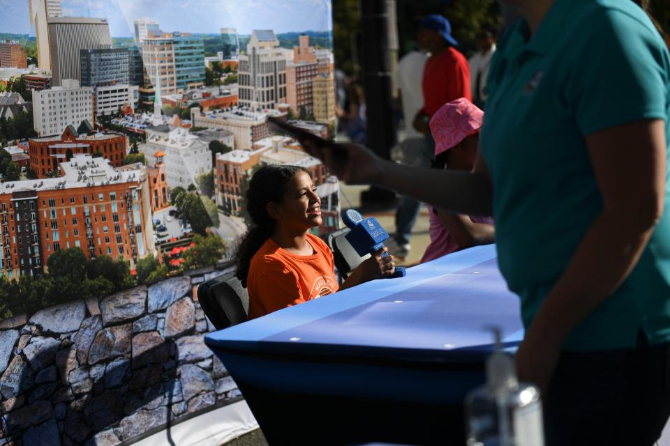 Ariana Hines, 10, pretends to be a news caster at WYFF's booth at Fall For Greenville on Saturday, Oct. 14, 2023 in downtown Greenville, S.C.