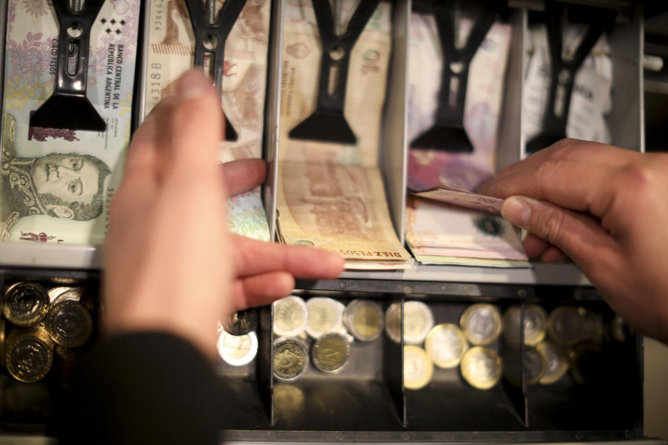 A man holds a 100 peso bill in the cashier of a restaurant in Buenos Aires, Argentina, Wednesday, Aug. 14, 2019. President Mauricio Macri announced economic relief for poor and working-class Argentines that include an increased minimum wage, reduced payroll taxes, a bonus for informal workers and a freeze in gasoline prices. The conservative leader said Wednesday he's acting in recognition of the "anger" Argentines expressed in Sunday's primary election, when Macri trailed his populist rival by 15 percentage points. (AP Photo/Natacha Pisarenko)