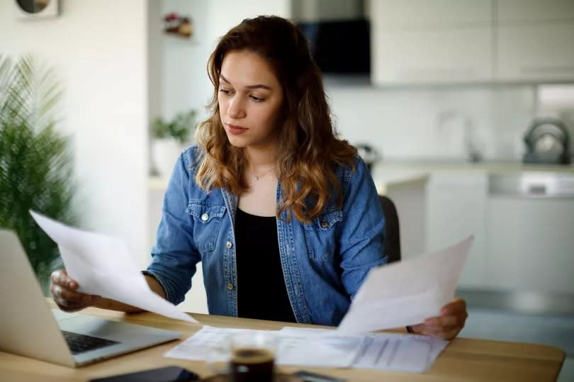 A woman checks bills at her laptop at home