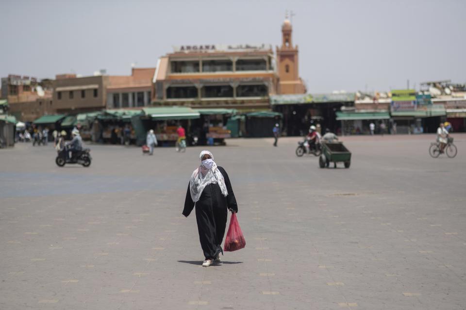 A woman walks with a grocery bag in the usually bustling landmark of Jemma el-Fnaa, in Marrakech, Morocco, Wednesday, July 22, 2020. Morocco's restrictions to counter the coronavirus pandemic have taken a toll on the carriage horses in the tourist mecca of Marrakech. (AP Photo/Mosa'ab Elshamy)