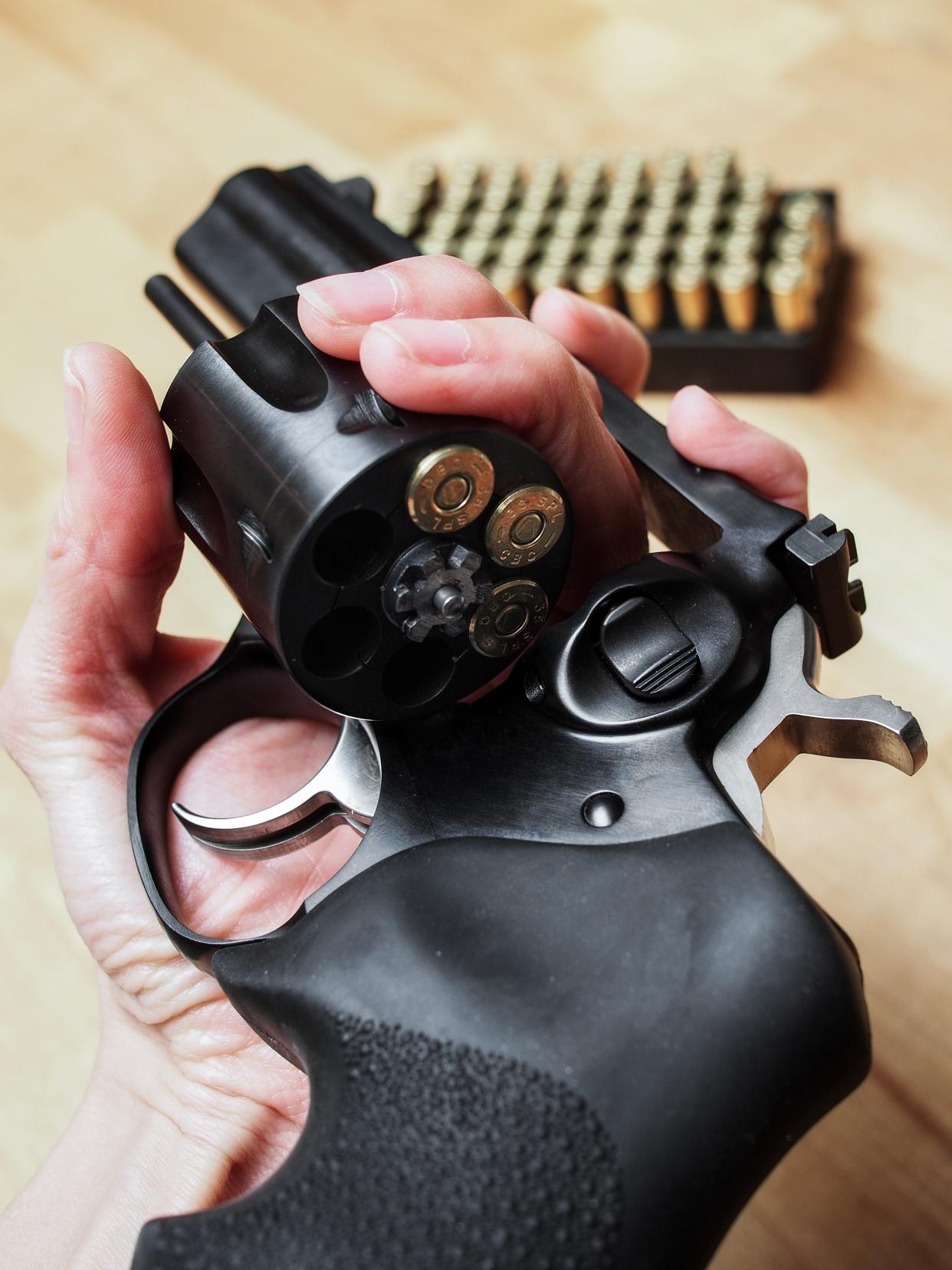 woman holding a black revolver with the cylinder open, half loaded with 38 special ammunition.