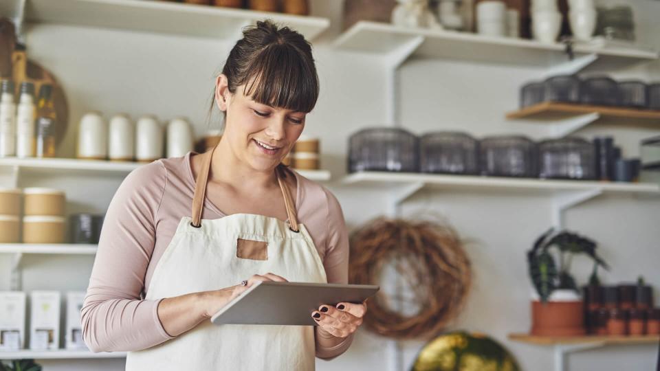 Smiling young female florist standing in her flower shop checking online orders with a digital tablet.