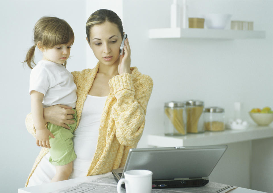 Woman looks furious on phone holding baby looking at laptop