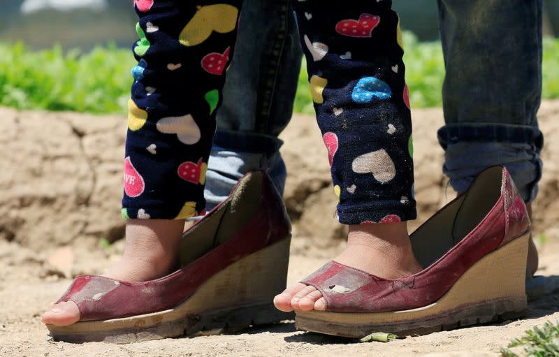 A Syrian refugee girl wears oversized shoes, as Lebanon extends a lockdown to combat the spread of the coronavirus disease (COVID-19) at a Syrian refugee camp in the Bekaa valley