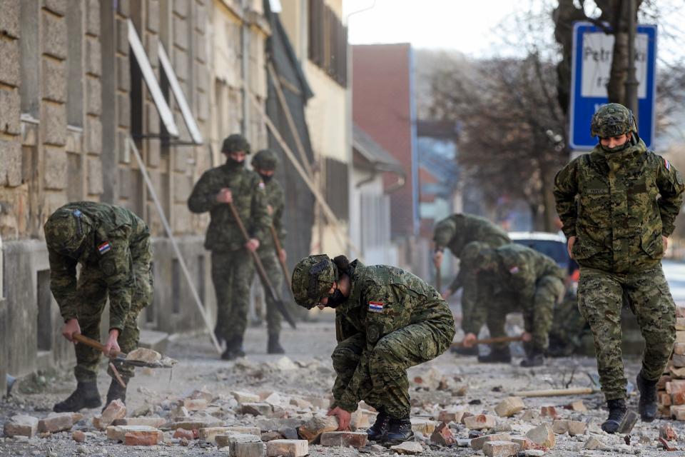 Croatian soldiers clean rubble in a street next to damaged buildings in Petrinja, some 50kms from Zagreb, after the town was hit by an earthquake of the magnitude of 6,4 on December 29, 2020. - The tremor, one of the strongest to rock Croatia in recent years, collapsed rooftops in Petrinja, home to some 20,000 people, and left the streets strewn with bricks and other debris. Rescue workers and the army were deployed to search for trapped residents, as a girl was reported dead. (Photo by Damir SENCAR / AFP) (Photo by DAMIR SENCAR/AFP via Getty Images)