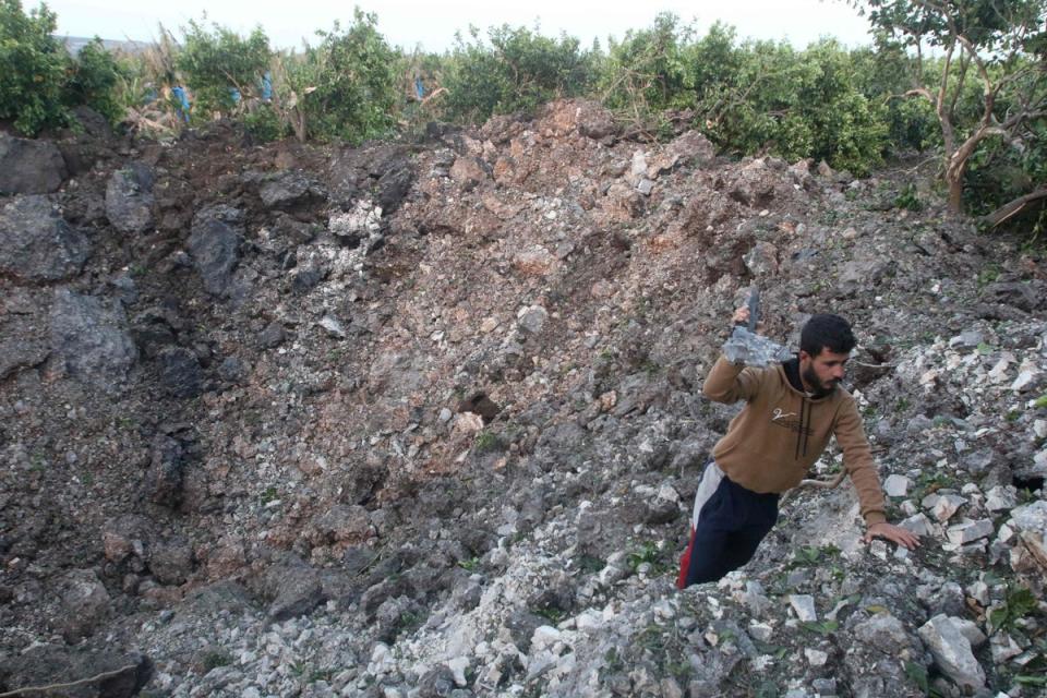 A man holds shrapnel in a crater left by a rocket following Israeli air strikes in Al Qulaylah (AFP via Getty Images)