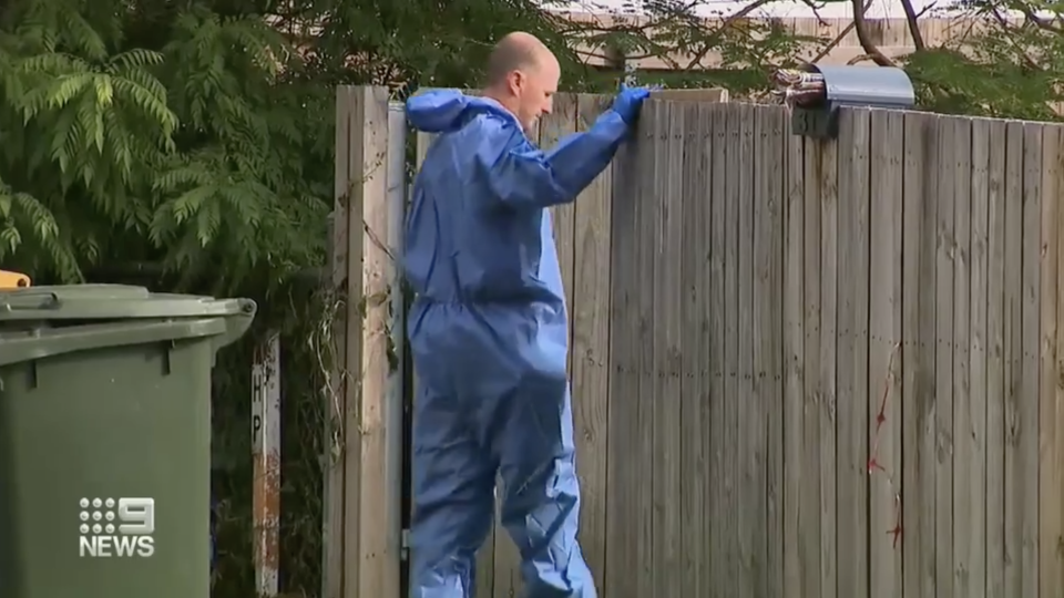 A forensic police officer stands at a fence outside a Stafford home.