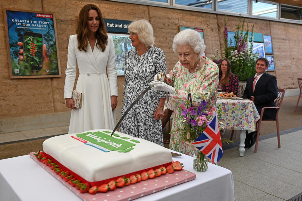 ST AUSTELL, ENGLAND - JUNE 11: Queen Elizabeth II (C) attempts to cut a cake with a sword, lent to her by The Lord-Lieutenant of Cornwall, Edward Bolitho, to celebrate of The Big Lunch initiative at The Eden Project during the G7 Summit on June 11, 2021 in St Austell, Cornwall, England. UK Prime Minister, Boris Johnson, hosts leaders from the USA, Japan, Germany, France, Italy and Canada at the G7 Summit. This year the UK has invited India, South Africa, and South Korea to attend the Leaders' Summit as guest countries as well as the EU. (Photo by Oli Scarff - WPA Pool / Getty Images)