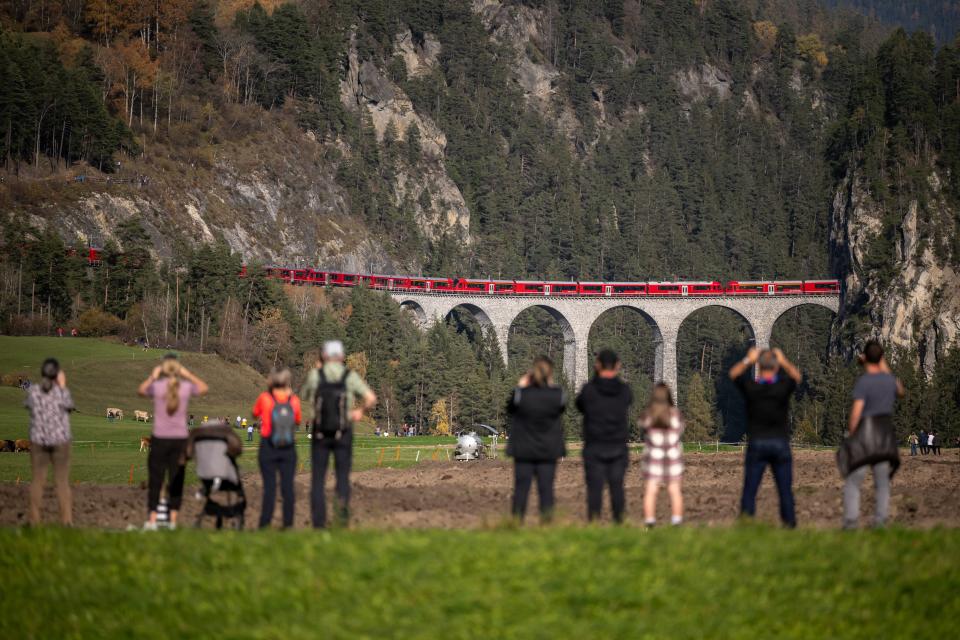 Members of the public capture images as a 1910-metre-long train with 100 cars passes the Landwasser Viaduct, after Bergun, on October 29, 2022, during a record attempt by the Rhaetian Railway (RhB) of the World's longest passenger train, to mark the Swiss railway operator's 175th anniversary. - The record attempt is carried out on the Albula Line, from Preda to Thusis, crossing one of the most spectacular railways in the world, recognised as a Unesco World Heritage Site.