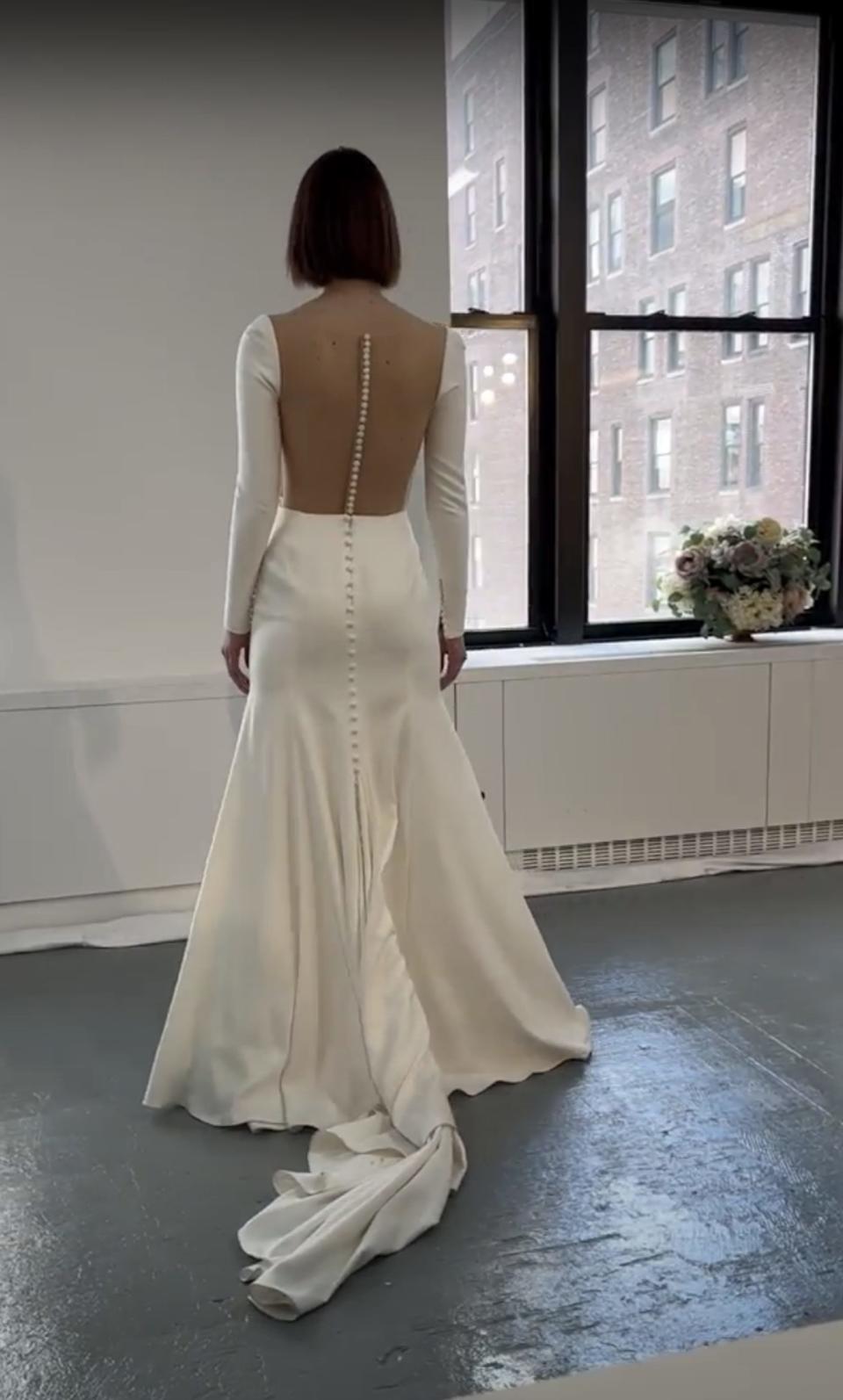 A woman poses in a wedding dress with buttons down the back.