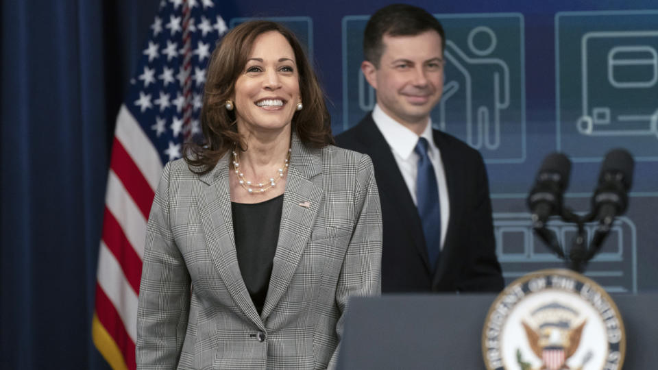 Vice President Kamala Harris and Secretary of Transportation Pete Buttigieg walk toward a podium.