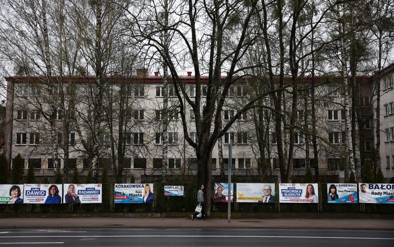 FILE PHOTO: Man walks in fonts of the election posters hanging on the fence, ahead of next weekend Polish local elections, in Szczytno,
