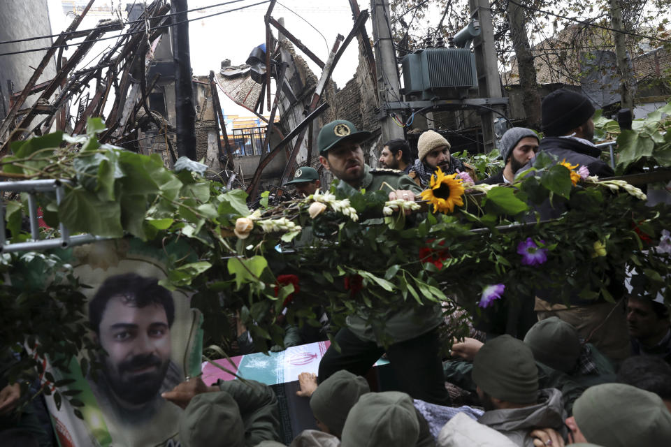 Mourners surround the flag-draped coffin of Revolutionary Guard member Morteza Ebrahimi, seen in a poster at the bottom left, during a funeral procession that passed protest-damaged buildings in the town of Shahriar, Iran, some 40 kilometers (25 miles) southwest of the capital, Tehran, Wednesday, Nov. 20, 2019. Ebrahimi was killed during protests over government-set fuel prices rising last week, demonstrations that quickly spiraled in violence. (AP Photo/Vahid Salemi)