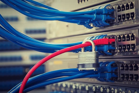 Many blue ethernet cables plugged into a rack of network switches. Among them, a padlock hangs on a single red cable.