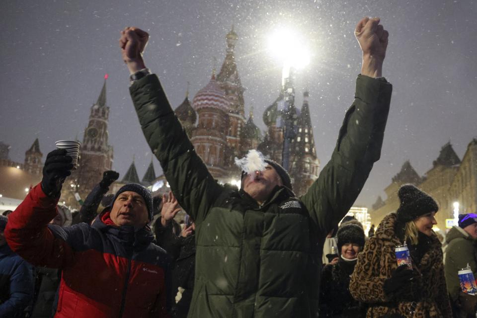 Un hombre en medio de una multitud alza los brazos cerca de la Plaza Roja, con la catedral de San Basilio --al centro-- y la torre Spasskaya --a la izquierda-- como fondo, para festejar el Año Nuevo luego de la medianoche, el lunes 1 de enero de 2024, en Moscú, Rusia. (AP Foto/Marina Lystseva)