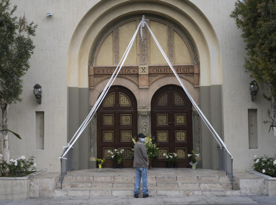 FILE - In this Sunday, April 12, 2020, file photo, a parishioner prays outside the closed doors decorated with Easter lily flowers at the Christ the King Church Roman Catholic Church in Los Angeles. A federal appeals court has denied a Southern California church's request to overturn the state's coronavirus restrictions barring worship services indoors during the coronavirus pandemic. The Sacramento Bee says Friday, Jan. 22, 2021, ruling by the 9th U.S. Circuit Court of Appeals leaves the door open for addressing Gov. Gavin Newsom administration's limits on church attendance if a California county is in a less-restrictive COVID-19 tier. (AP Photo/Damian Dovarganes, File)