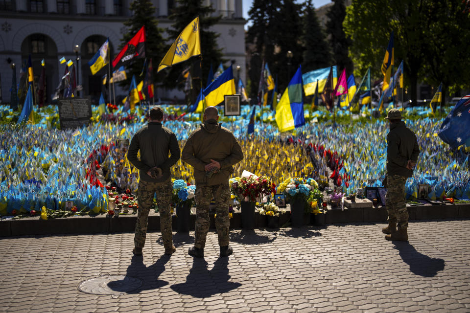 Ukrainian service men stand next to Ukrainian flags and photographs placed in memory of civilians and soldiers killed during the war, at the Independence square in central Kyiv, Saturday, April 20, 2024. (AP Photo/Francisco Seco)