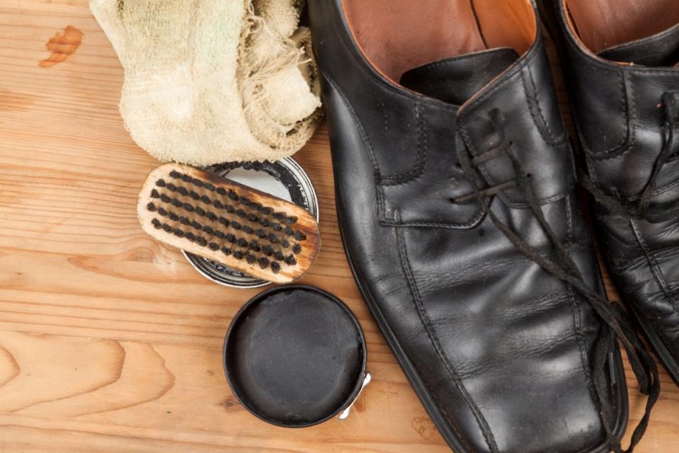 Black shoe polish and brush next to black shoes