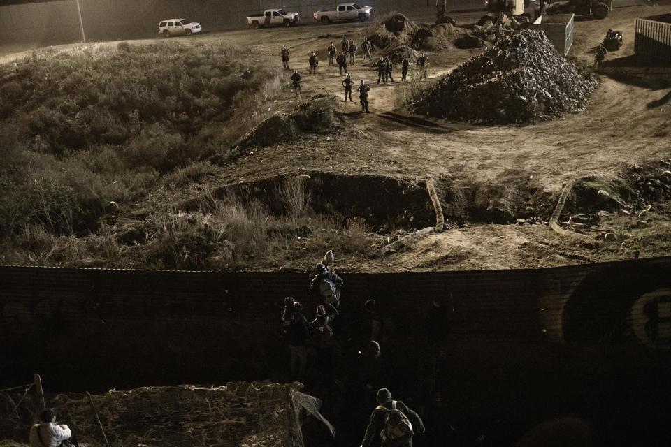 Migrants climb the border fence in front of U.S. Border Protection officers as they make an attempt to get into the U.S. side to San Diego, Calif., from Tijuana, Mexico, Tuesday, Jan. 1, 2019. Discouraged by the long wait to apply for asylum through official ports of entry, many migrants from recent caravans are choosing to cross the U.S. border wall and hand themselves in to border patrol agents. (AP Photo/Daniel Ochoa de Olza)