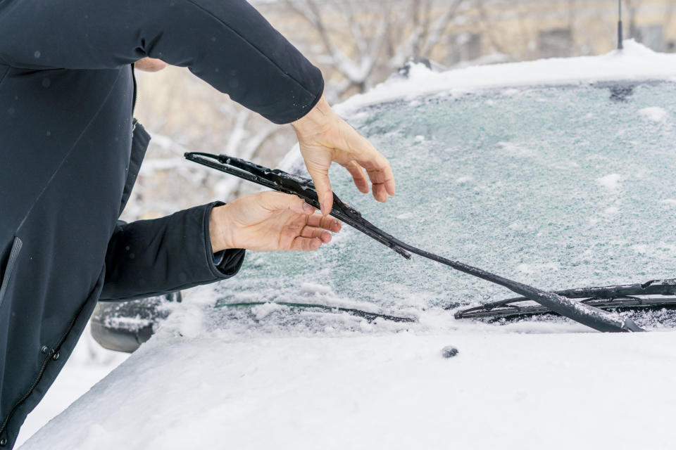 man adjusting and cleaning windshield wipers of car in snowy weather