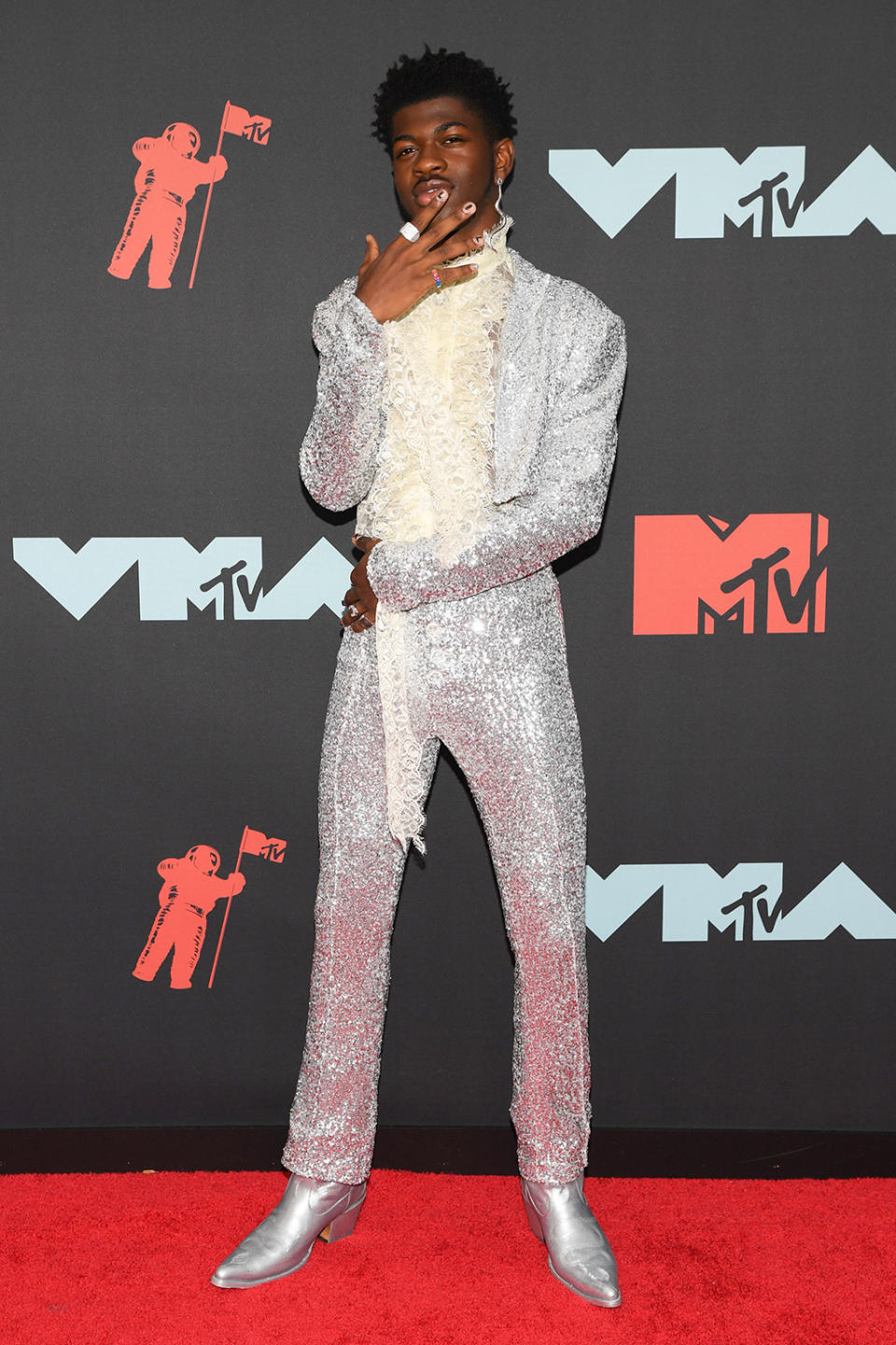 Lil Nas X wears a silver suit with cowboy boots at the MTV VMAs. - Credit: Andrew H. Walker/Shutterstock