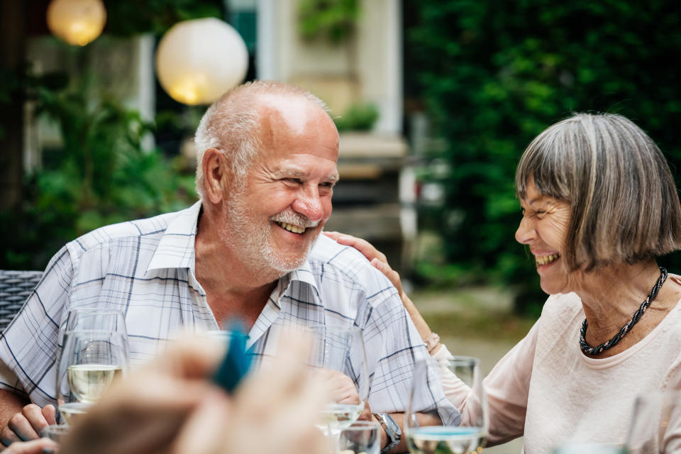 An elderly couple smiling and drinking at a family barbecue in a courtyard.