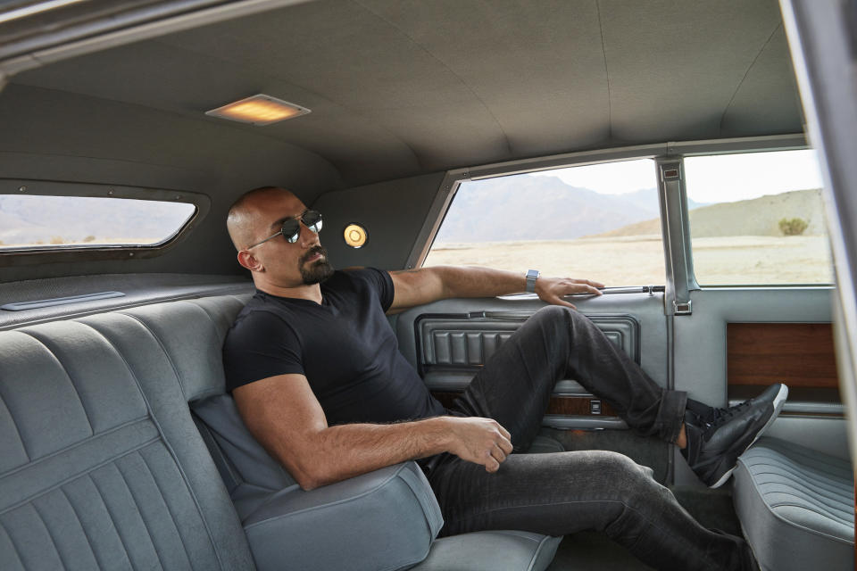 A man wearing sunglasses and lounging in the back of a spacious and expensive car