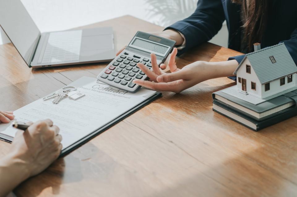 a woman with a calculator holding it up for a person signing papers with keys on the documents